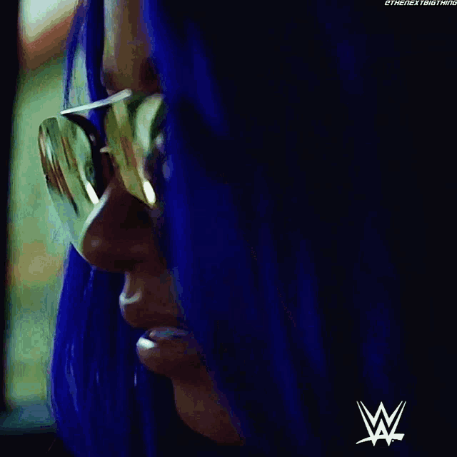 a close up of a woman with blue hair wearing sunglasses and a w logo