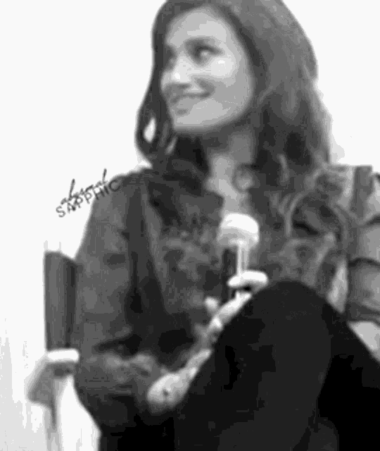 a woman is sitting in a chair holding a microphone and smiling ..