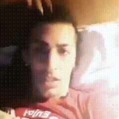 a man in a red shirt is laying in bed with his hand on his head .
