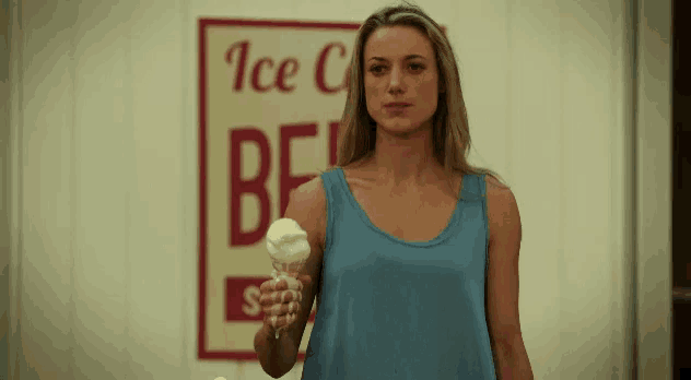 a woman holding an ice cream cone in front of an ice cream shop sign