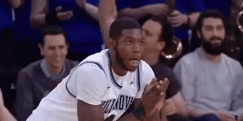 a basketball player is sitting on the floor with his hands folded in front of a crowd of people .