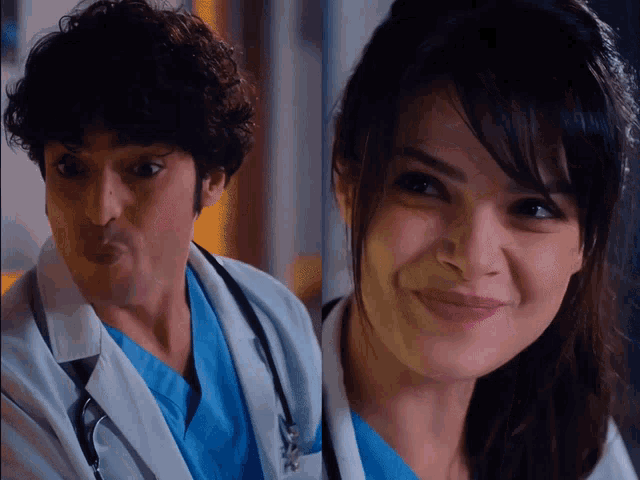 a man in a lab coat making a face and a woman in a blue scrub smiling