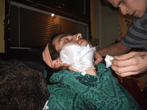 a man is shaving another man 's face with shaving cream on it