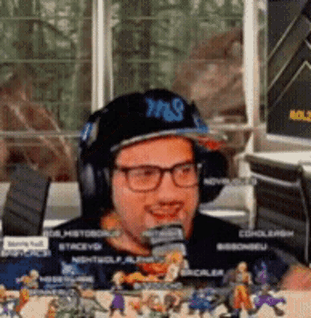a man wearing headphones and a hat with the letter s on it is sitting in front of a table full of toy figures