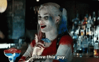 a woman in a harley quinn costume is sitting at a bar holding a drink and saying i love this guy
