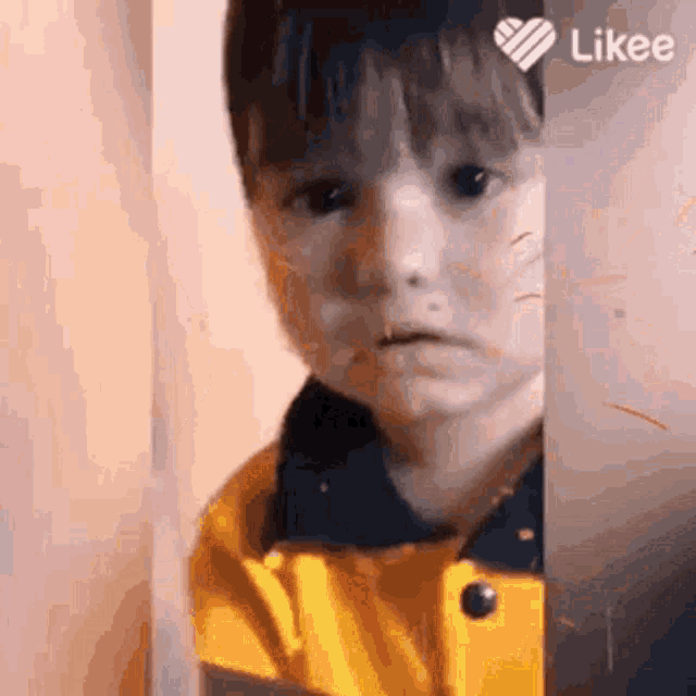 a young boy wearing a yellow jacket is making a sad face .