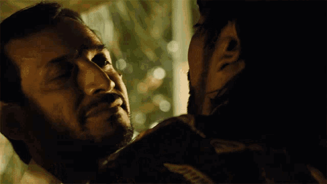 a man with a beard is touching another man 's face in a dark room