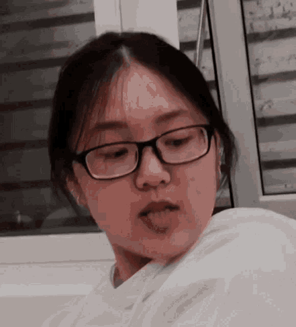 a young woman wearing glasses and a white hoodie is looking at the camera .