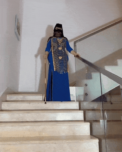 a woman in a blue and gold dress is walking down a set of stairs