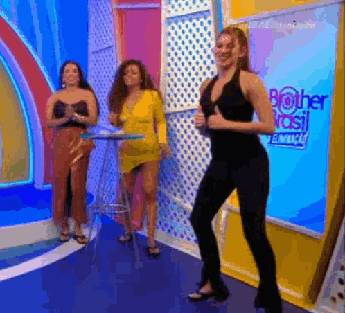 a woman in a black jumpsuit is dancing on a stage in front of two other women .