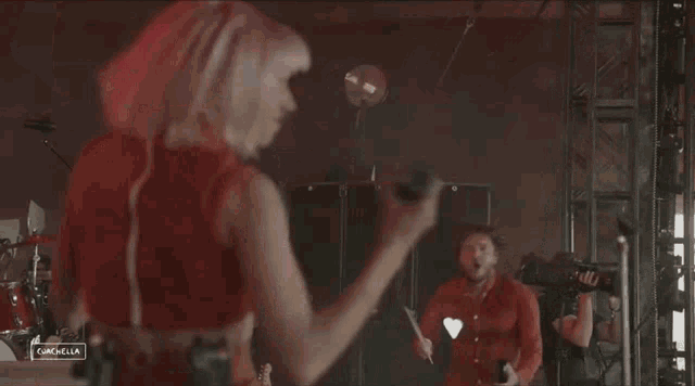 a woman in a red top sings into a microphone while a man in a red shirt watches