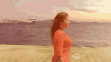 a woman in a red dress is walking on a beach with a cruise ship in the background .