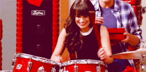 a woman playing drums with a man holding a gift box