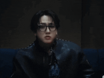 a man wearing glasses and a black leather jacket is sitting on a couch .