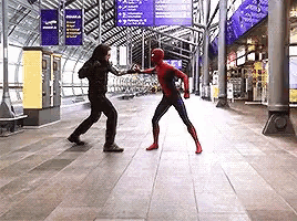 a man in a spiderman costume is fighting another man in a black suit
