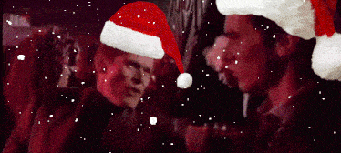 two men wearing santa hats are standing in the snow