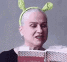 a woman is wearing shrek ears and reading a book .