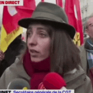 a woman wearing a hat and scarf is talking into a microphone at a protest .
