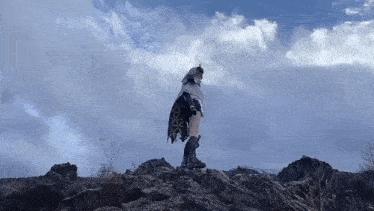a person in a costume is standing on top of a rocky hill holding a sword .