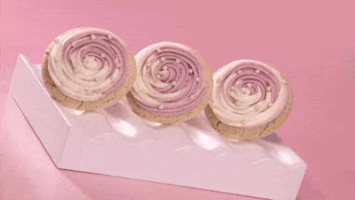 three cupcakes with pink frosting and sprinkles on a white plate