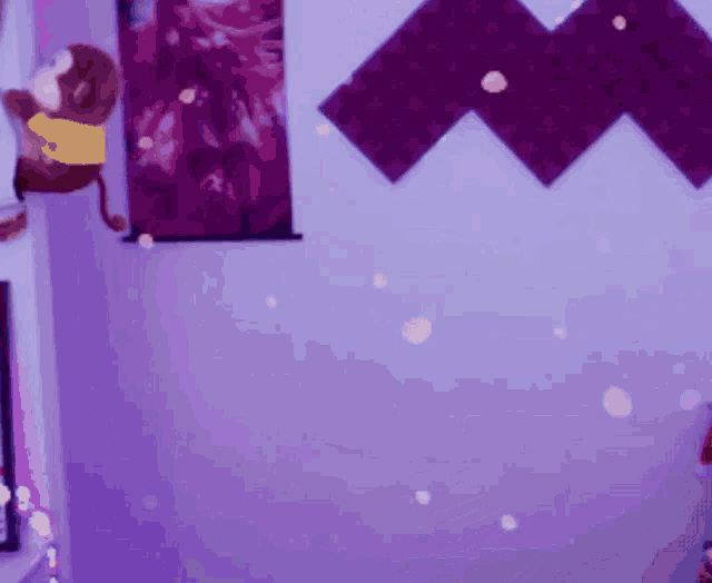 a stuffed monkey in a yellow shirt is sitting on a shelf in front of a purple wall