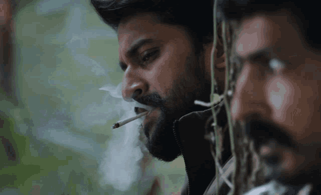 a man with a beard is smoking a cigarette while another man looks on