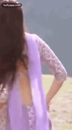 a woman in a purple saree is standing in a field .