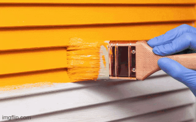 a person wearing blue gloves is using a brush to paint a yellow wall