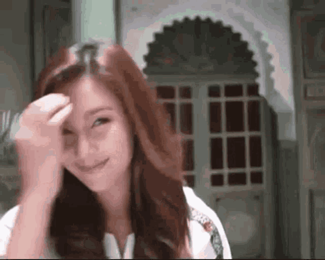 a woman with long red hair is smiling and touching her hair .