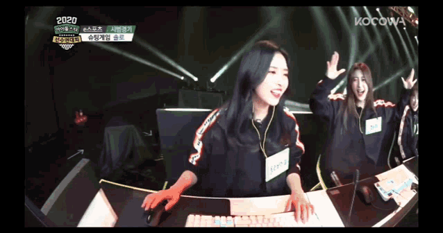 a group of girls are sitting at a desk with their hands in the air with the year 2020 on the bottom