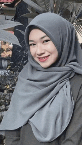 a woman wearing a gray hijab is smiling and looking at the camera