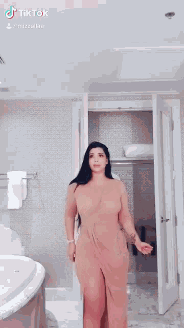 a woman in a dress is standing in a bathroom next to a bathtub .
