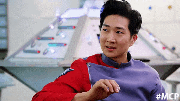 a man in a red shirt and purple shirt is sitting in front of a control panel .