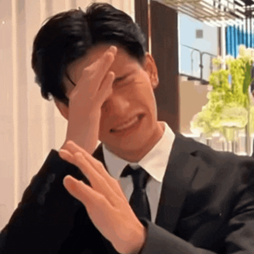 a man in a suit and tie is covering his face with his hands