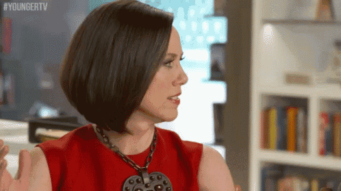 a woman wearing a red dress and a necklace is talking to someone .