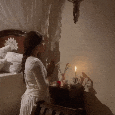 a woman is praying in front of a cross and candle