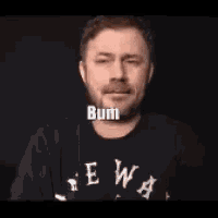 a man with a beard is wearing a shirt that says bum .