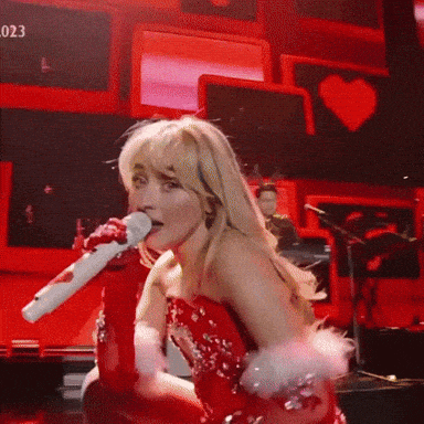 a woman in a red dress is singing into a microphone with the number 023 in the background