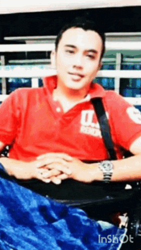 a man in a red polo shirt and a watch is sitting in a chair .