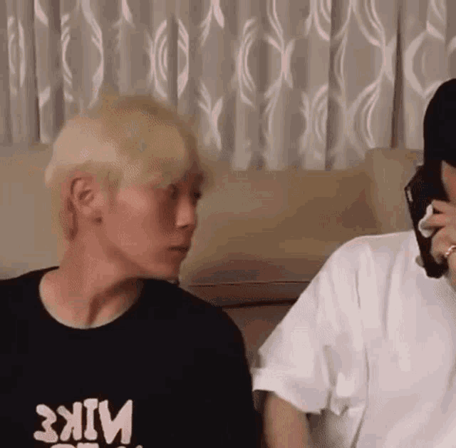 a man with blonde hair is sitting on a couch next to another man .