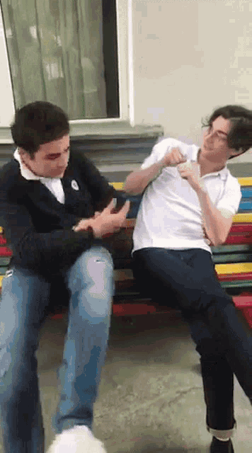 two young men are sitting on a bench and one of them is holding the other 's hand