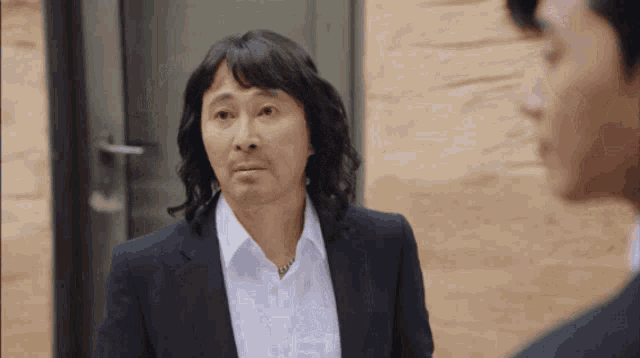 a man with long hair and a mustache is wearing a suit and white shirt