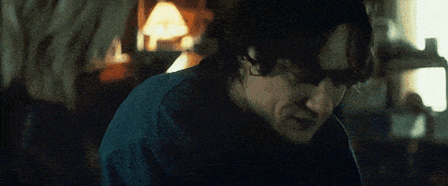 a man in a blue shirt is sitting in a dark room with his eyes closed .