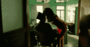 a woman in a red dress is kissing a man in a black chair