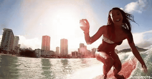 a woman in a bikini is riding a wave on a surfboard with a city skyline in the background