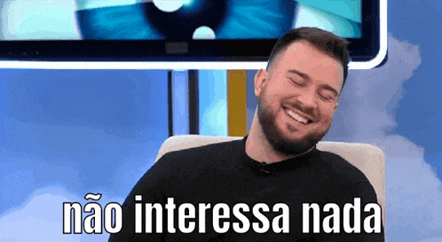 a man with a beard is smiling in front of a tv screen that says " não interessa nada "