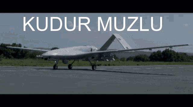 a military plane is sitting on a runway with the words kudur muzlu written above it
