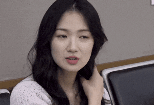 a woman with long black hair is sitting in a chair and touching her hair