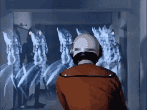 a man in a helmet stands in front of a group of aliens in a hallway .