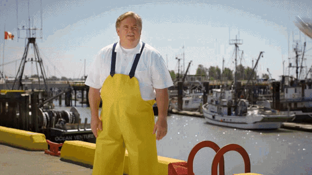 a man wearing yellow overalls stands in front of a boat that says ocean venture